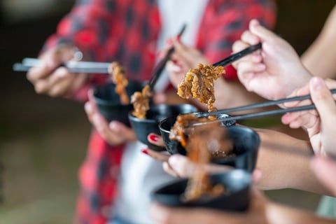 People enjoying a meal, using chopsticks to serve themselves a barbecue meal from small black bowls