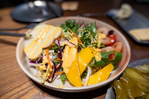 Fresh salad with mango slices, shrimp, and creamy dressing on wooden table