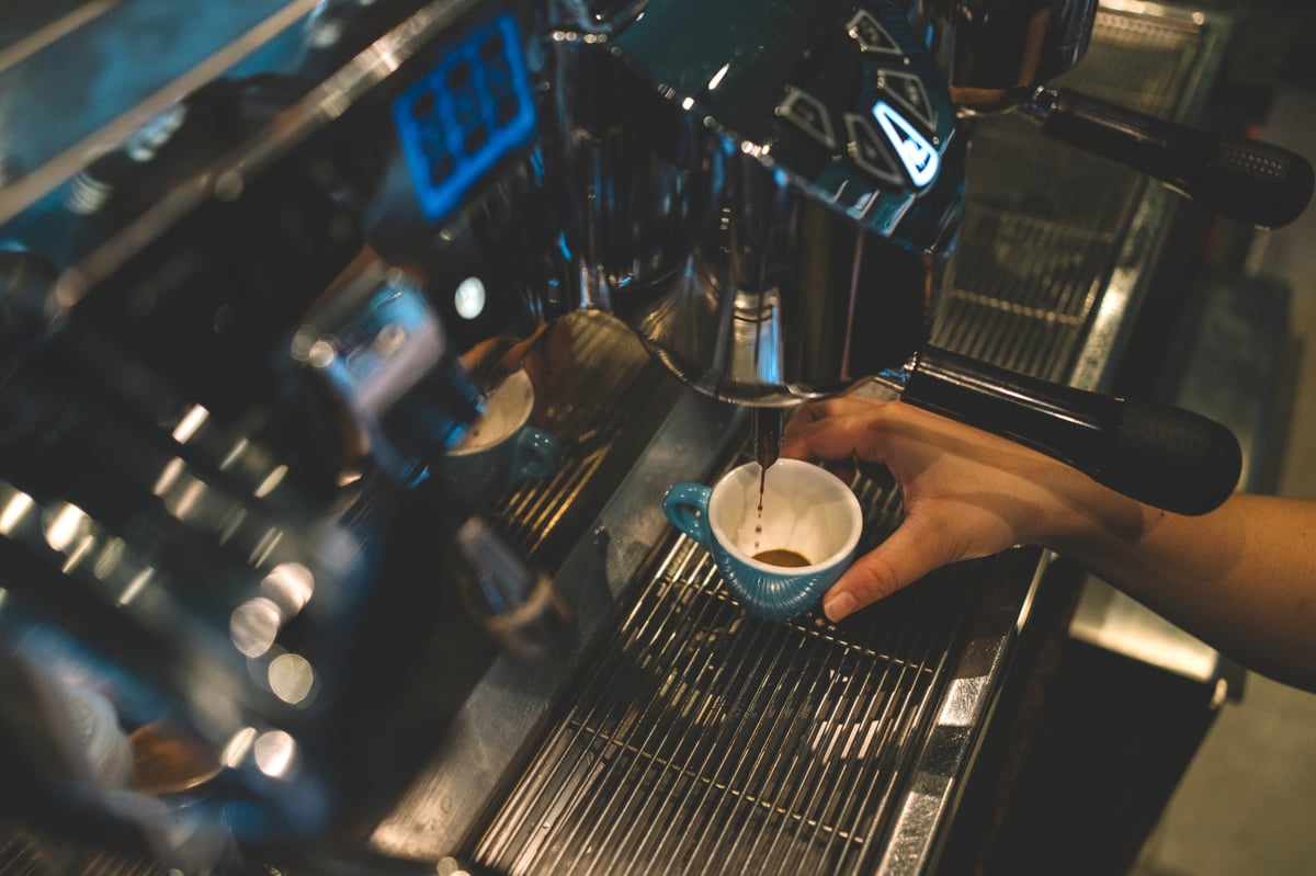 Barista holding a small cup under a professional espresso machine during coffee extraction.