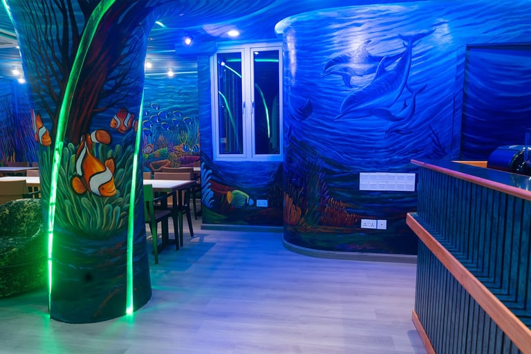 Underwater-themed attraction with blue lighting, murals of sea creatures, illuminated green plant column, and railings along the walkway