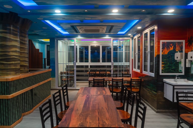 Modern restaurant interior with blue ceiling lights, wood tables, black chairs, and contemporary wall art in red and green tones