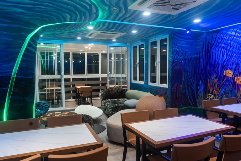 Modern lounge area with neon green and blue lighting, white tables, wooden chairs, and floor-to-ceiling windows overlooking a city at night