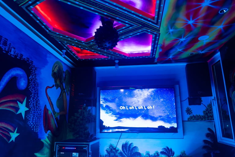 Neon-lit gaming room with glowing blue and purple lights, wall art, and a monitor displaying a sky scene