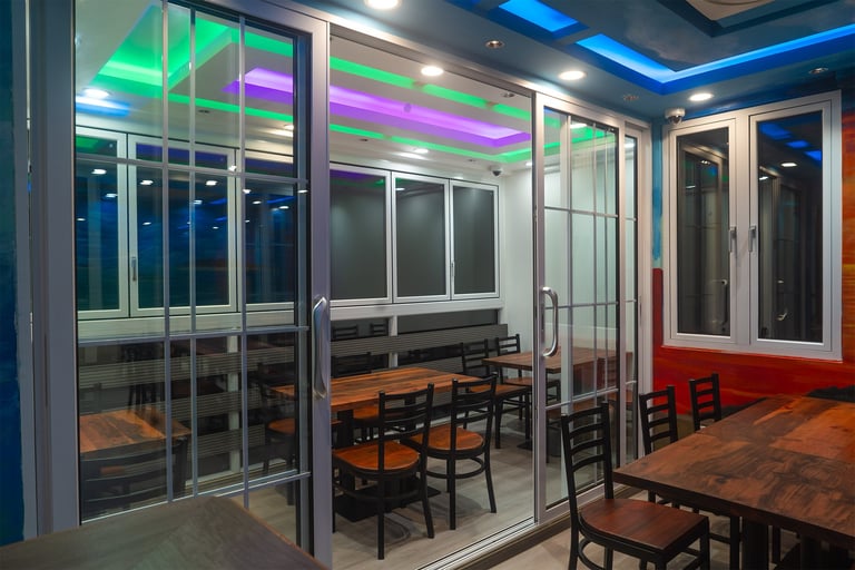 Modern interior space with glass partition walls, wooden tables and black chairs, neon green and purple lighting fixtures on ceiling