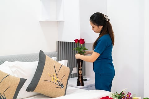 Woman in blue shirt arranging red flowers in a vase on a bedroom nightstand