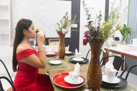 Woman in red dress holding yellow flower, standing at decorated dining table with floral centerpieces and place settings