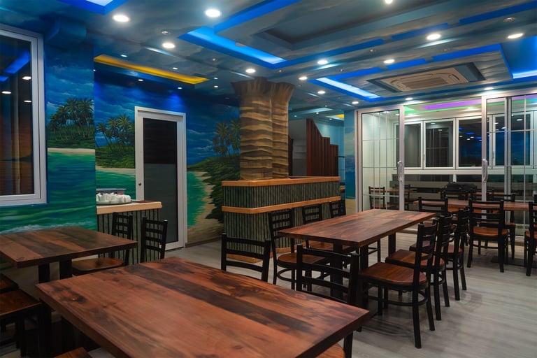 Modern office break room with blue ceiling, wooden tables, chairs, and nature-themed wall murals with landscape artwork