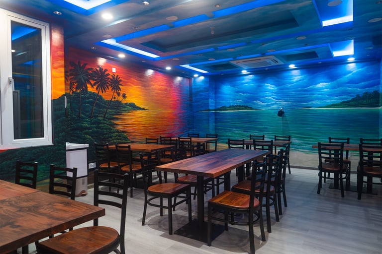 Modern dining space with wooden tables and black chairs, illuminated by blue overhead lighting and tropical sunset mural on wall