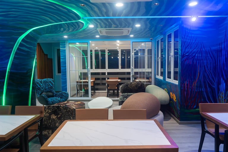 Modern office break room with blue neon lighting, white tables, curved seating areas, and floor-to-ceiling windows overlooking city lights