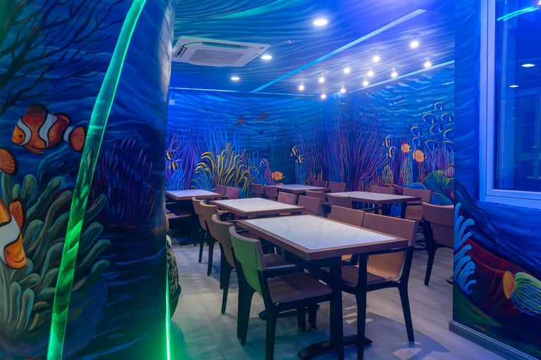 Underwater-themed restaurant with blue lighting, neon green accents, dining tables, and colorful fish murals on walls