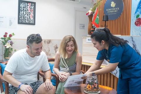 Three people examining documents together at a table in an office or community space with decorative artwork on the walls