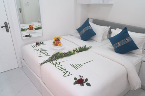 Modern bedroom with white bed decorated with thank you message in flowers and leaves, blue pillows, small breakfast tray, and mirror on wall